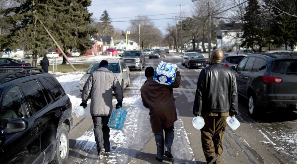 Flint residents Marcus Shelton, from left, Roland Young, and Darius Martin walk on an ice-covered street as they retrieve free water. AP