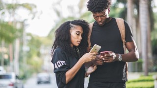 Image of two young Black adults using their cell phones.