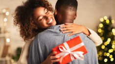 Thankful afro woman with christmas gift hugging husband at home